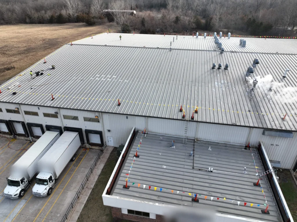 Aerial view of a large standing seam metal roof and office wing before a retrofit