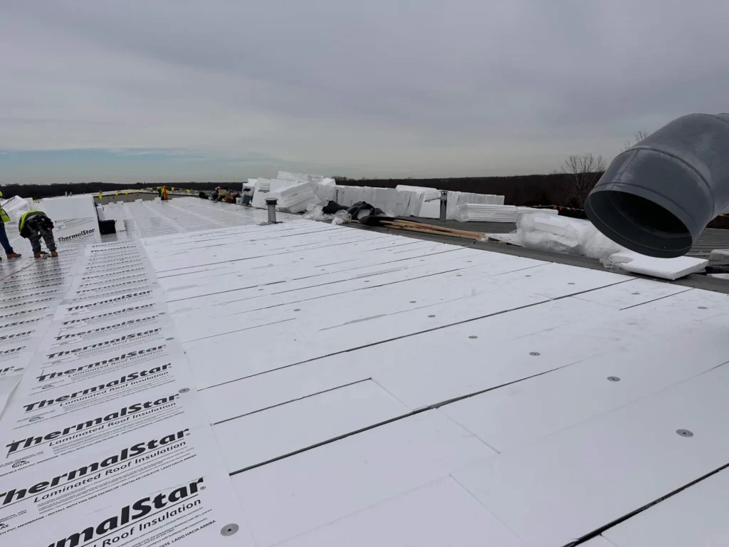 Flute-fill insulation and laminated insulation board in progress on a large metal roof