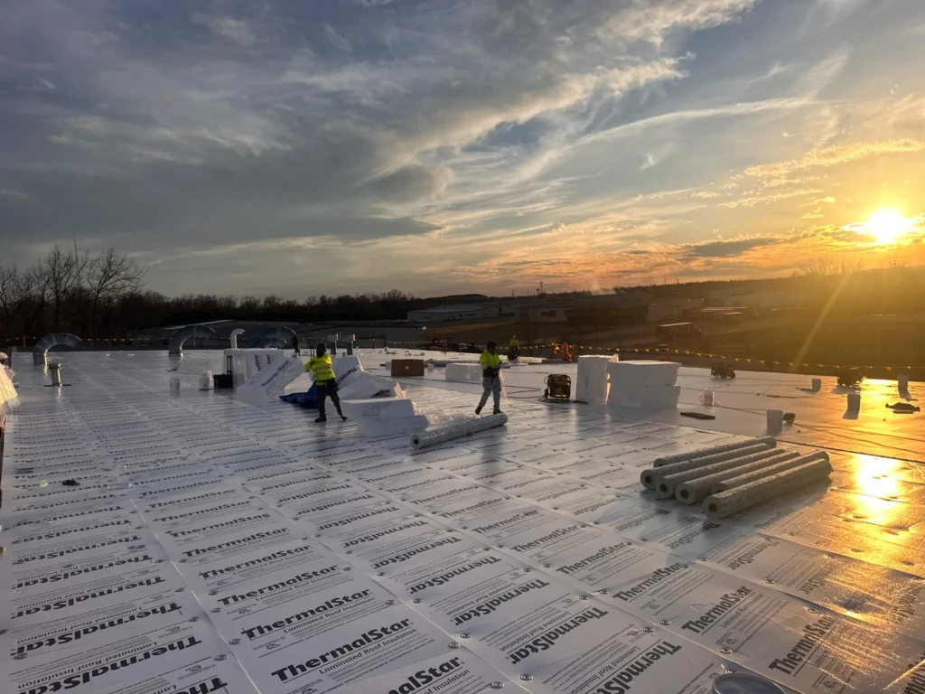 Crew installing ThermalStar coverboard at sunset during a metal roof retrofit