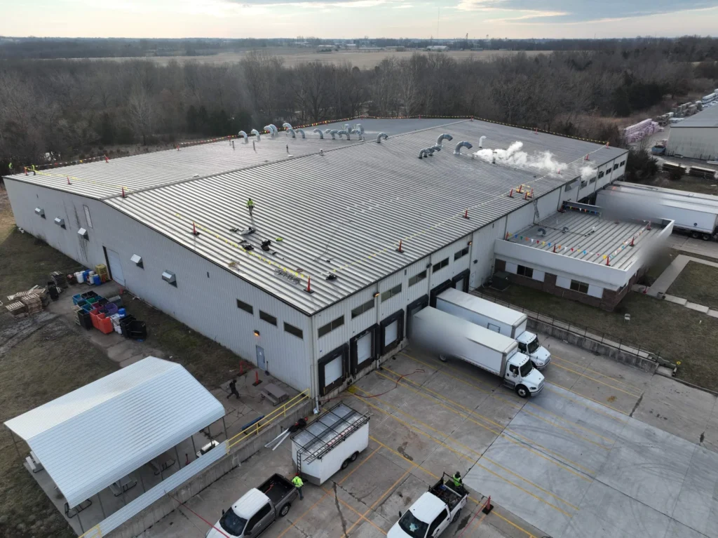 Aerial view of crews setting up perimeter safety lines on a large standing seam metal roof