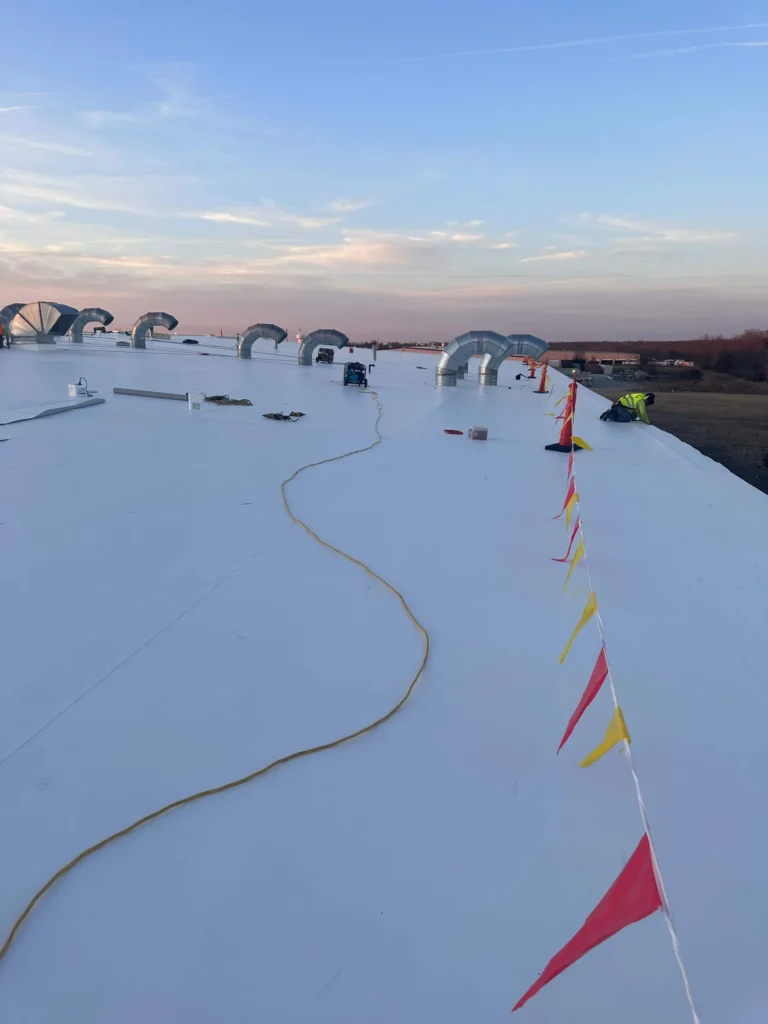 Roofing membrane positioned along the roof edge with crew finishing the perimeter