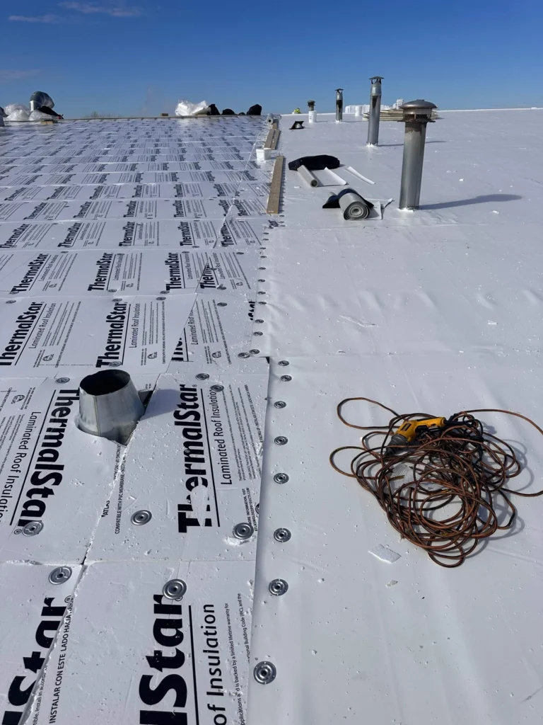 Roofing membrane being rolled out and fastened over ThermalStar coverboard